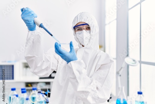 Young blonde woman scientist wearing security uniform pouring liquid on sample at laboratory