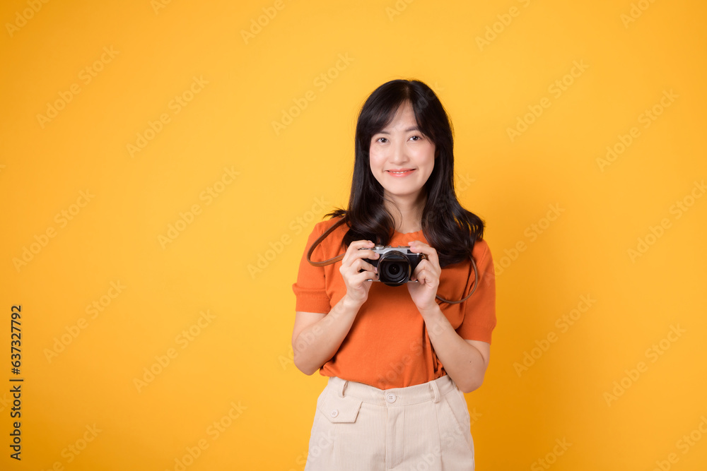 Positive lady tourist isolated on yellow background, holding a camera, excited for a memorable trip.