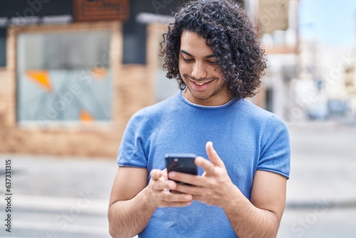Young latin man smiling confident using smartphone at street