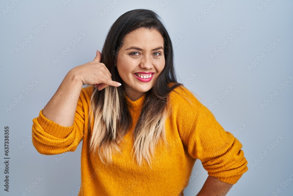 Young hispanic woman standing over isolated background smiling doing phone gesture with hand and fingers like talking on the telephone. communicating concepts. Young hispanic woman standing over isolated background smiling doing phone gesture with hand and fingers like talking on the telephone. communicating concepts.