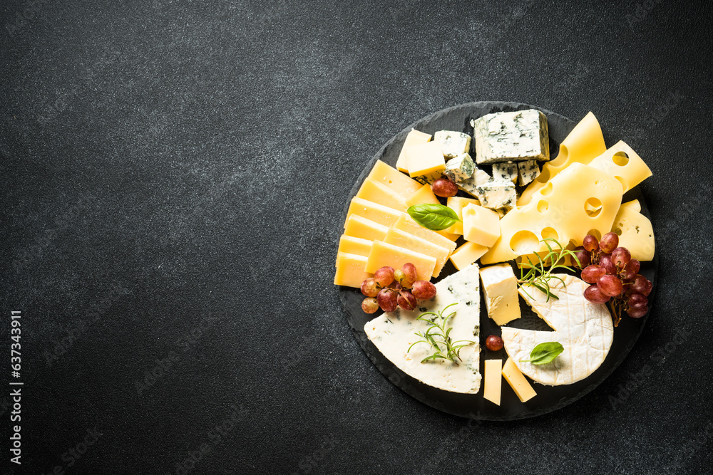 Cheese platter with craft cheese assortment and grape at black background. Top view with copy space.