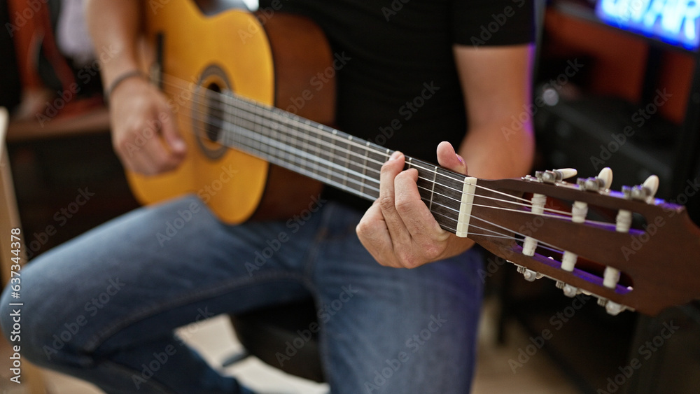 Obraz premium Young hispanic man musician playing classical guitar at music studio
