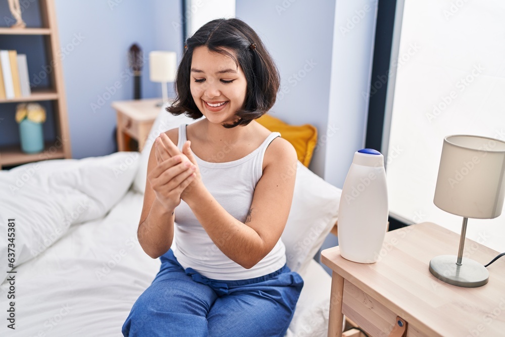 Young woman applying lotion on hands sitting on bed at bedroom Young woman applying lotion on hands sitting on bed at bedroom