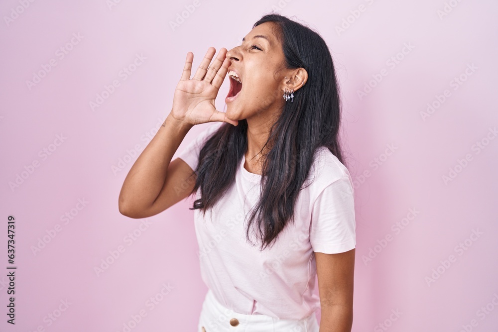 Young hispanic woman standing over pink background shouting and screaming loud to side with hand on mouth. communication concept. Young hispanic woman standing over pink background shouting and screaming loud to side with hand on mouth. communication concept.