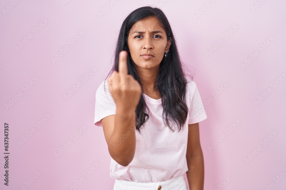 Young hispanic woman standing over pink background showing middle finger, impolite and rude fuck off expression Young hispanic woman standing over pink background showing middle finger, impolite and rude fuck off expression