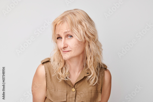 Portrait of blonde mature woman suspiciously looking at camera isolated on white studio background, squinting incredulously photo