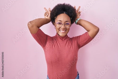 Beautiful african woman with curly hair standing over pink background posing funny and crazy with fingers on head as bunny ears  smiling cheerful