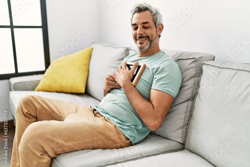 Middle age grey-haired man hugging picture sitting on sofa at home