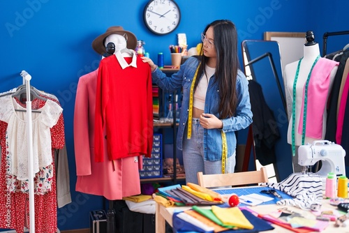 Young chinese woman tailor holding t shirt at clothing factory