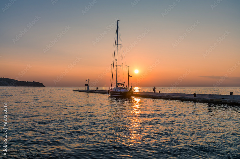 A view at sunset towards a yacht moored on a jetty in the harbour in Izola, Slovenia in summertime
