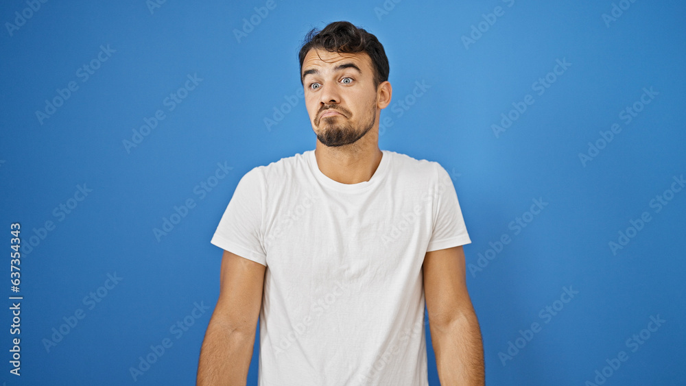 Young hispanic man standing clueless over isolated blue background Young hispanic man standing clueless over isolated blue background