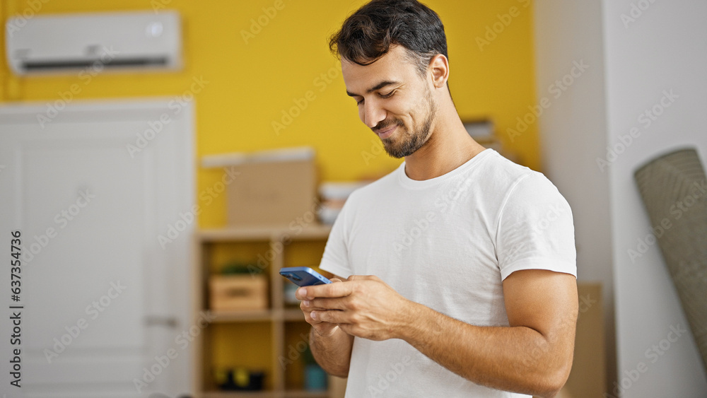 Young hispanic man using smartphone standing at new home Young hispanic man using smartphone standing at new home