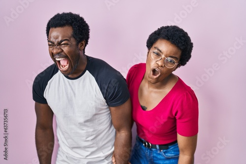 Young african american couple standing over pink background angry and mad screaming frustrated and furious, shouting with anger. rage and aggressive concept.