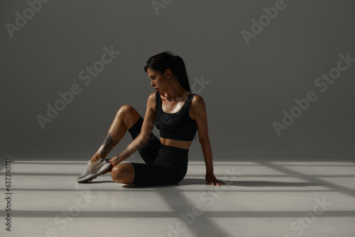 a tanned sports girl in a black suit is training in a yoga class in a fitness studio. white room. morning workout. warm-up