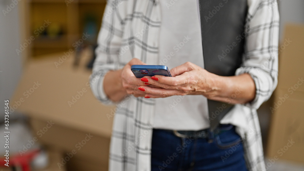 Middle age woman using smartphone holding clipboard at new home