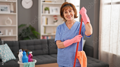 Middle age woman professional cleaner holding mop stick smiling home photo