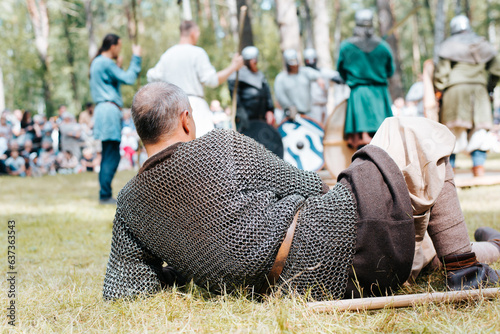 Back view of a tired warrior in chain mail resting on the grass in the forest