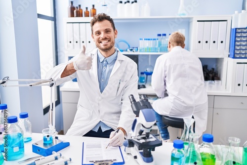 Hispanic man and woman working at scientist laboratory smiling happy and positive  thumb up doing excellent and approval sign