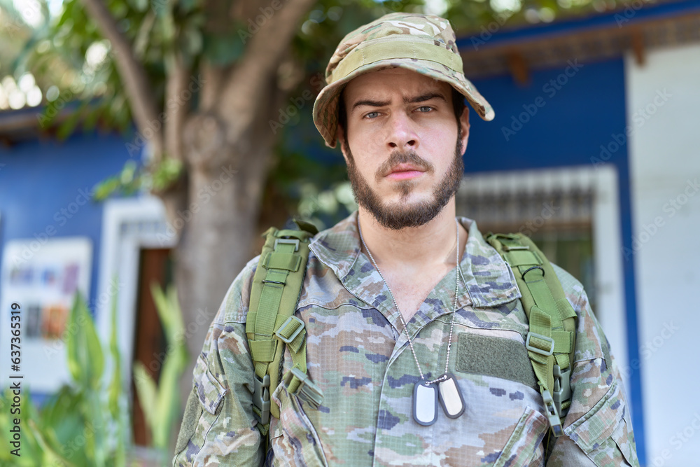 Young hispanic man wearing camouflage army uniform outdoors with serious expression on face. simple and natural looking at the camera.