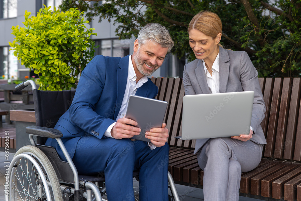 Businessman in wheelchair with female partner using laptop and tablet for working on joint project