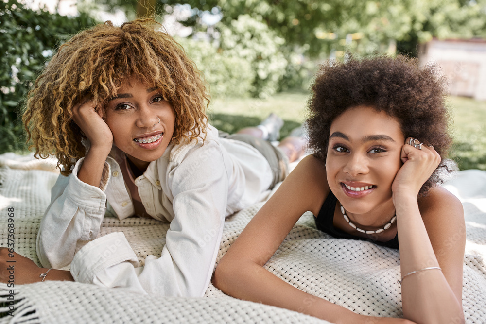 leisure in summer park, happy african american girlfriends laying on blanket and looking at camera leisure in summer park, happy african american girlfriends laying on blanket and looking at camera