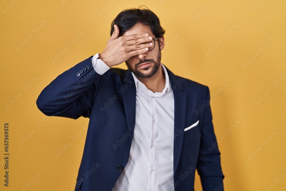 Handsome latin man standing over yellow background smiling and laughing with hand on face covering eyes for surprise. blind concept. Handsome latin man standing over yellow background smiling and laughing with hand on face covering eyes for surprise. blind concept.