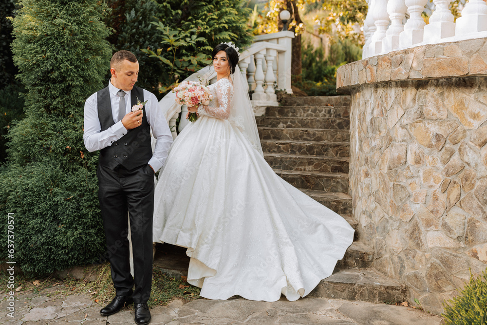 a beautiful bride in a chic wedding dress and an elegant groom stand on ancient steps in the park a beautiful bride in a chic wedding dress and an elegant groom stand on ancient steps in the park