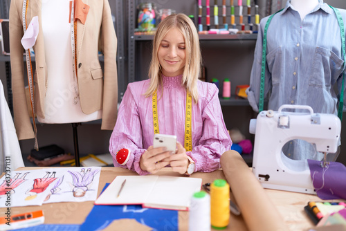 Young blonde woman tailor smiling confident using smartphone at tailor shop