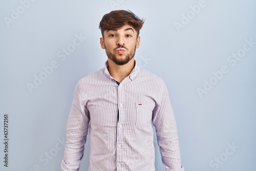 Arab man with beard standing over blue background looking at the camera blowing a kiss on air being lovely and sexy. love expression.