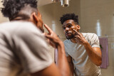 Homem negro olhando no espelho do banheiro durante sua rotina matinal em casa.