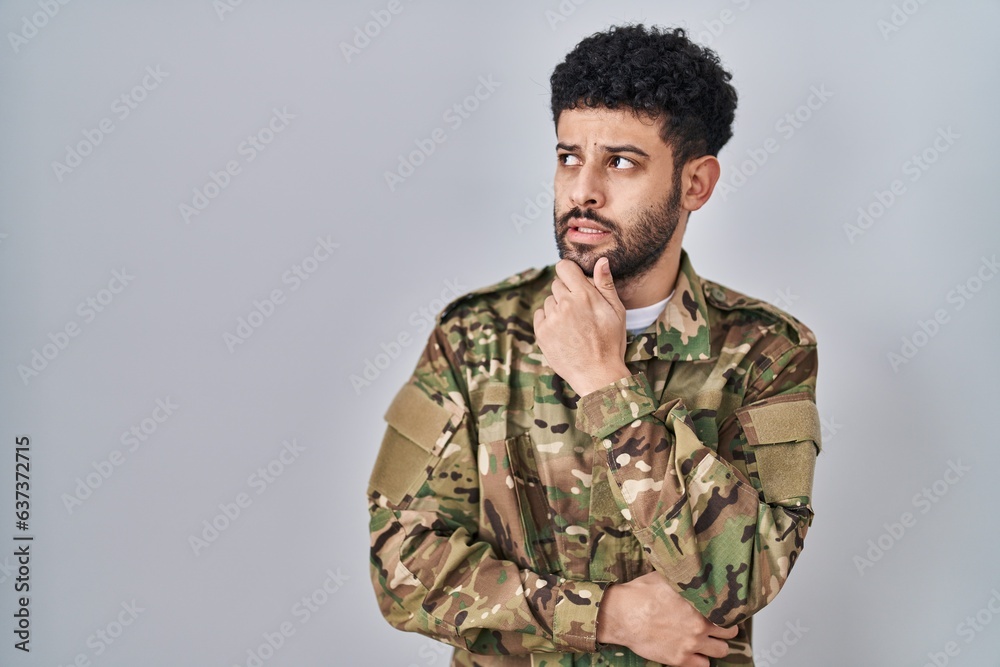 Arab man wearing camouflage army uniform thinking worried about a question, concerned and nervous with hand on chin