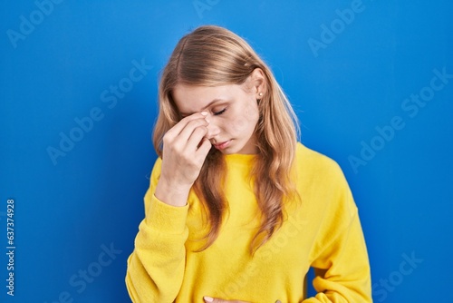 Young caucasian woman standing over blue background tired rubbing nose and eyes feeling fatigue and headache. stress and frustration concept.