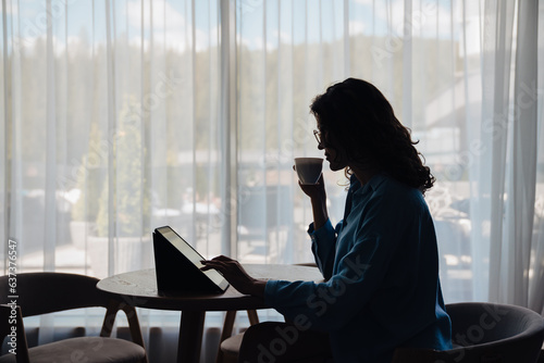 Young woman drinking coffee and using tablet while sitting at home
