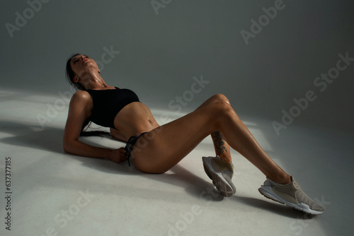 Pretty dark-haired girl posing for a fitness photo shoot in the studio. She is dressed in tight shorts and a crop top, and her poses convey a sense of strength, athleticism and fitness. Tan