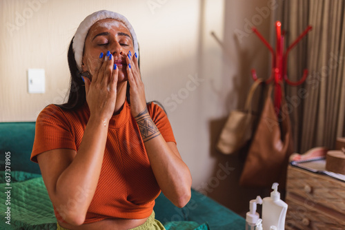 Bild auf Leinwand Jovem mulher indigena, sentada na cama, aplicando hidratante no rosto