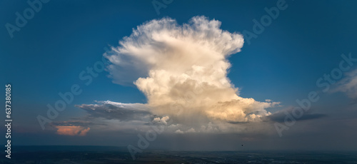 Panoramic aerial shot of cumulonimbus capillatus, a huge storm cloud cumulonimbus with dense cirrus clouds above against a blue sky and the silhouette of a small hot air balloon. photo