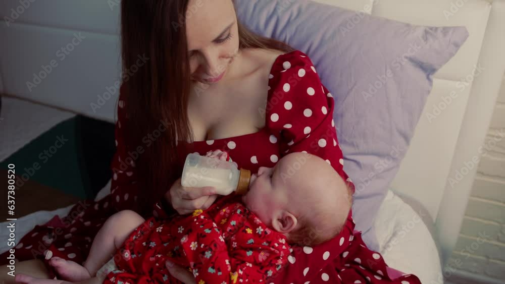 Young mother feeding her baby with a bottle of milk on the bed Young mother feeding her baby with a bottle of milk on the bed