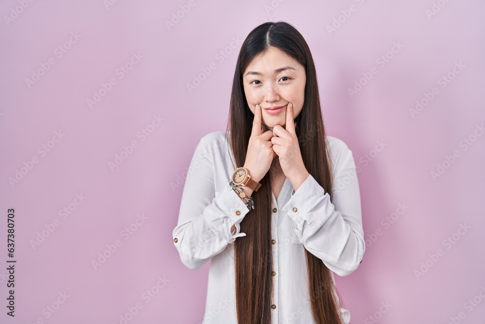 Chinese young woman standing over pink background smiling with open mouth, fingers pointing and forcing cheerful smile Chinese young woman standing over pink background smiling with open mouth, fingers pointing and forcing cheerful smile