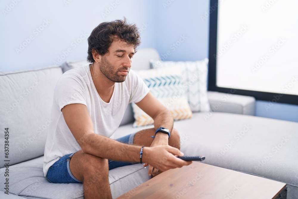 Young hispanic man watching movie sitting on sofa at home
