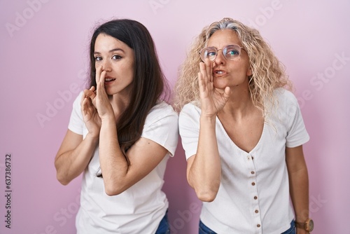 Mother and daughter standing together over pink background hand on mouth telling secret rumor, whispering malicious talk conversation