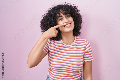 Young middle east woman standing over pink background pointing with hand finger to face and nose, smiling cheerful. beauty concept © Krakenimages.com