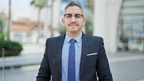 Young hispanic man business worker standing with serious face at street