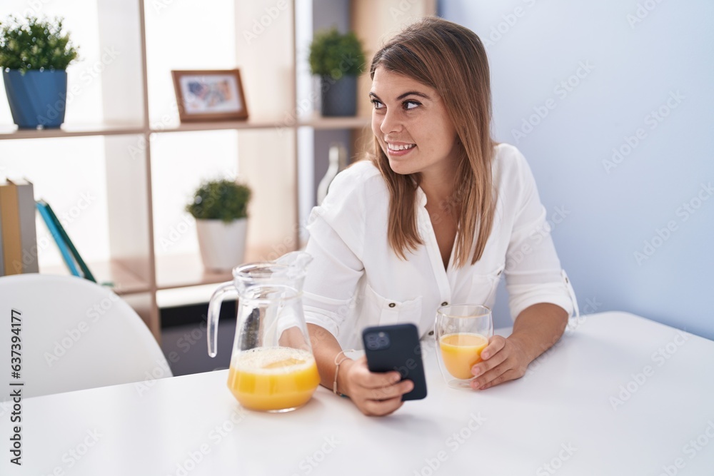 Young woman using smartphone drinking orange juice at home Young woman using smartphone drinking orange juice at home