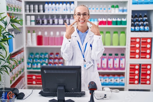 Young caucasian woman working at pharmacy drugstore smiling cheerful showing and pointing with fingers teeth and mouth. dental health concept.