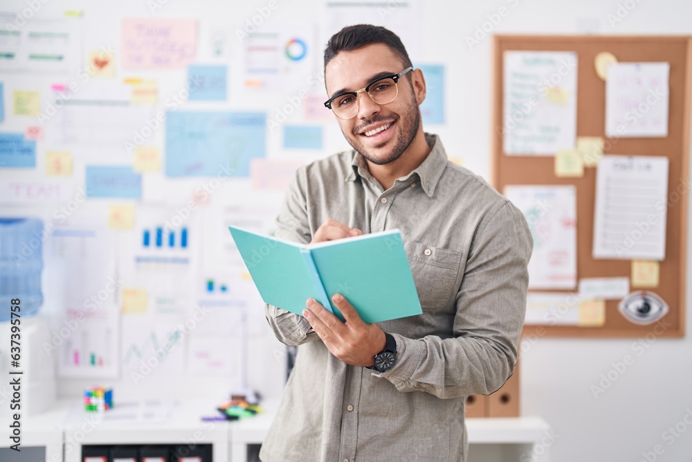 Young hispanic man business worker writing on notebook at office