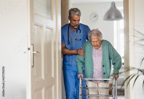 Caregiver helping senior woman to walk in her home with walker. photo