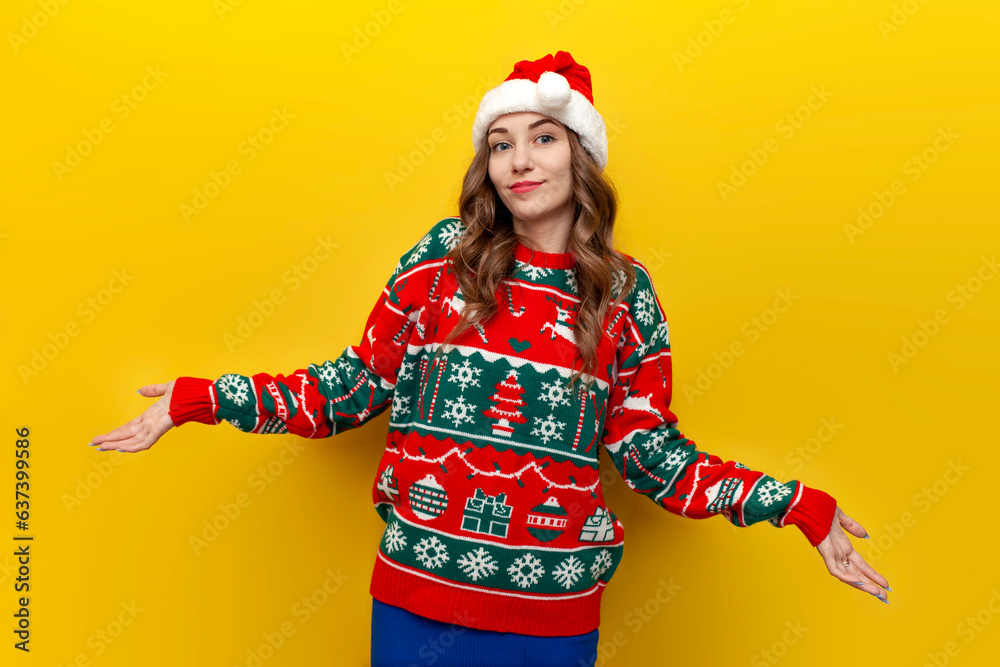 insecure girl in christmas sweater and santa claus hat shrugging her shoulders on yellow isolated background insecure girl in christmas sweater and santa claus hat shrugging her shoulders on yellow isolated background