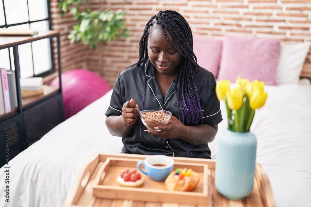 African american woman having gift breakfast sitting on bed at bedroom