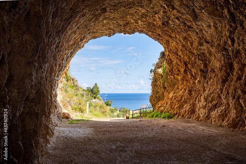 At the entrance of the Zingaro National Park you have a view from a rock tunnel with gravel ends to the blue sea and the blue sky.