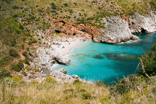 A secluded bay with white sand and turquoise waters in the Mediterranean Sea between the rocks of the Zingaro National Park in Sicily in the sun
